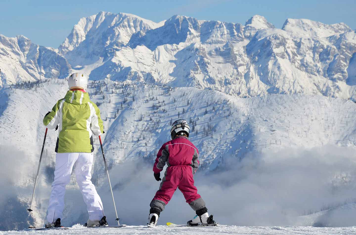 Erwachsene Person mit Kind in Begleitung auf Skiern am Berg