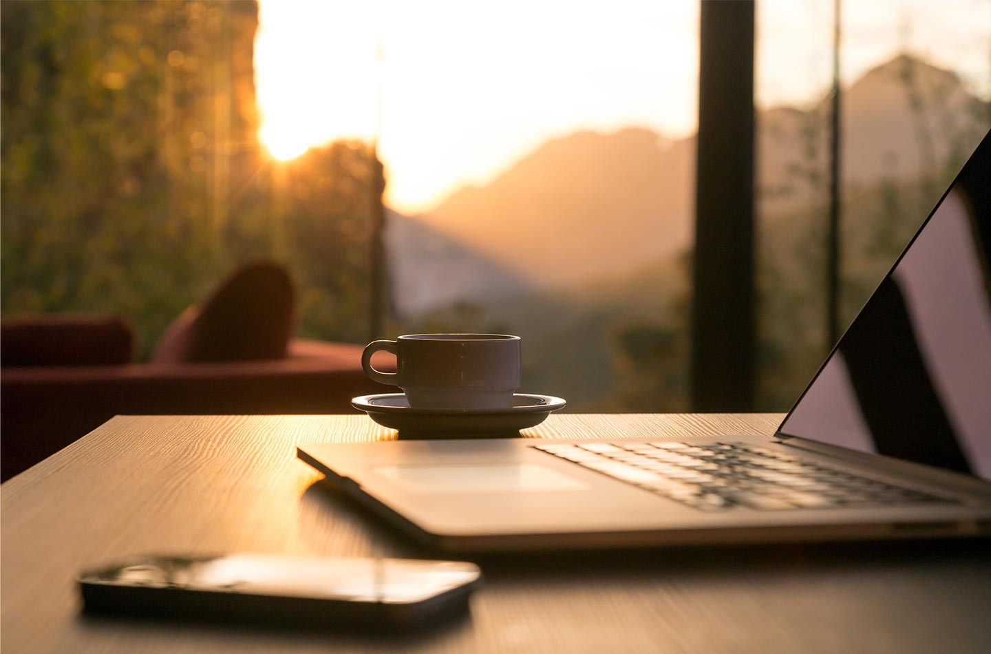 Laptop mit Kaffeetasse im Schein der aufgehenden Sonne. 