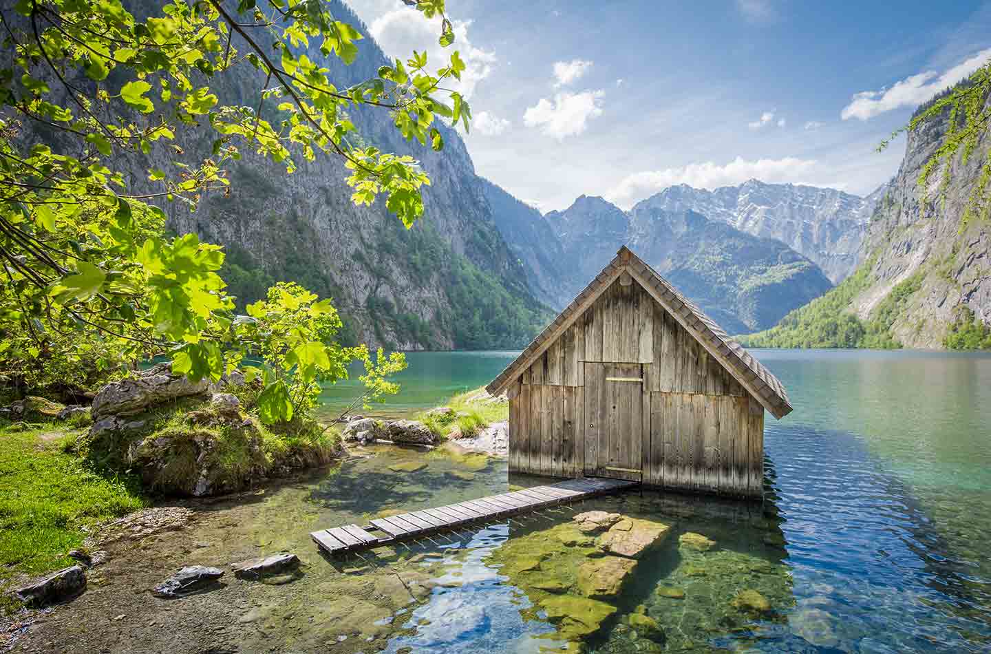 Hütte mit Steg auf Bergsee. Im Hintergrund ist der See umrahmt von den steilen Felskanten der Alpen