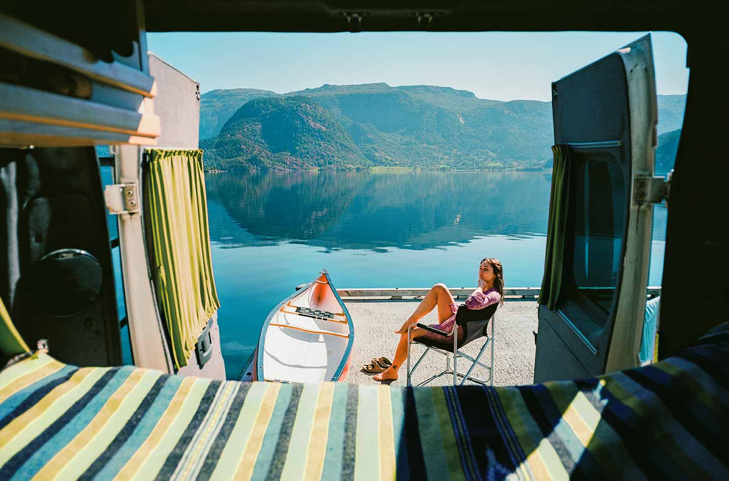 Frau sitzt in Norwegen an einem Fjord. Das Bild ist aus ihrem Van herausfotografiert. Ein Boot liegt bereit. 