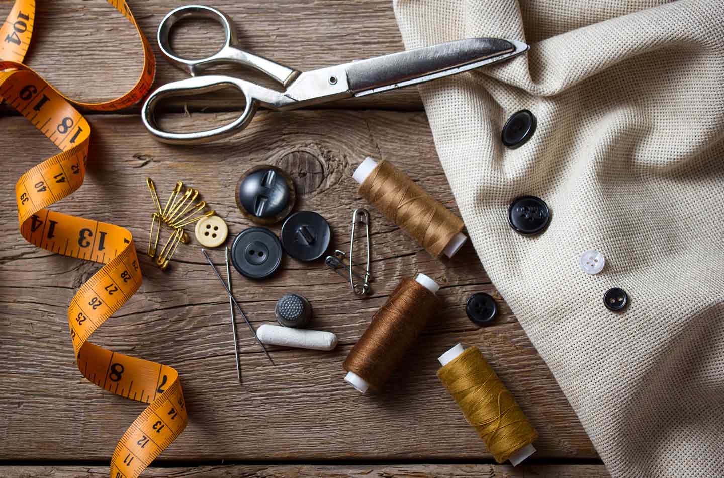 Utensilien zum Nähen auf einem Holztisch mit Stoff, Knöpfen, Maßband und Schere.