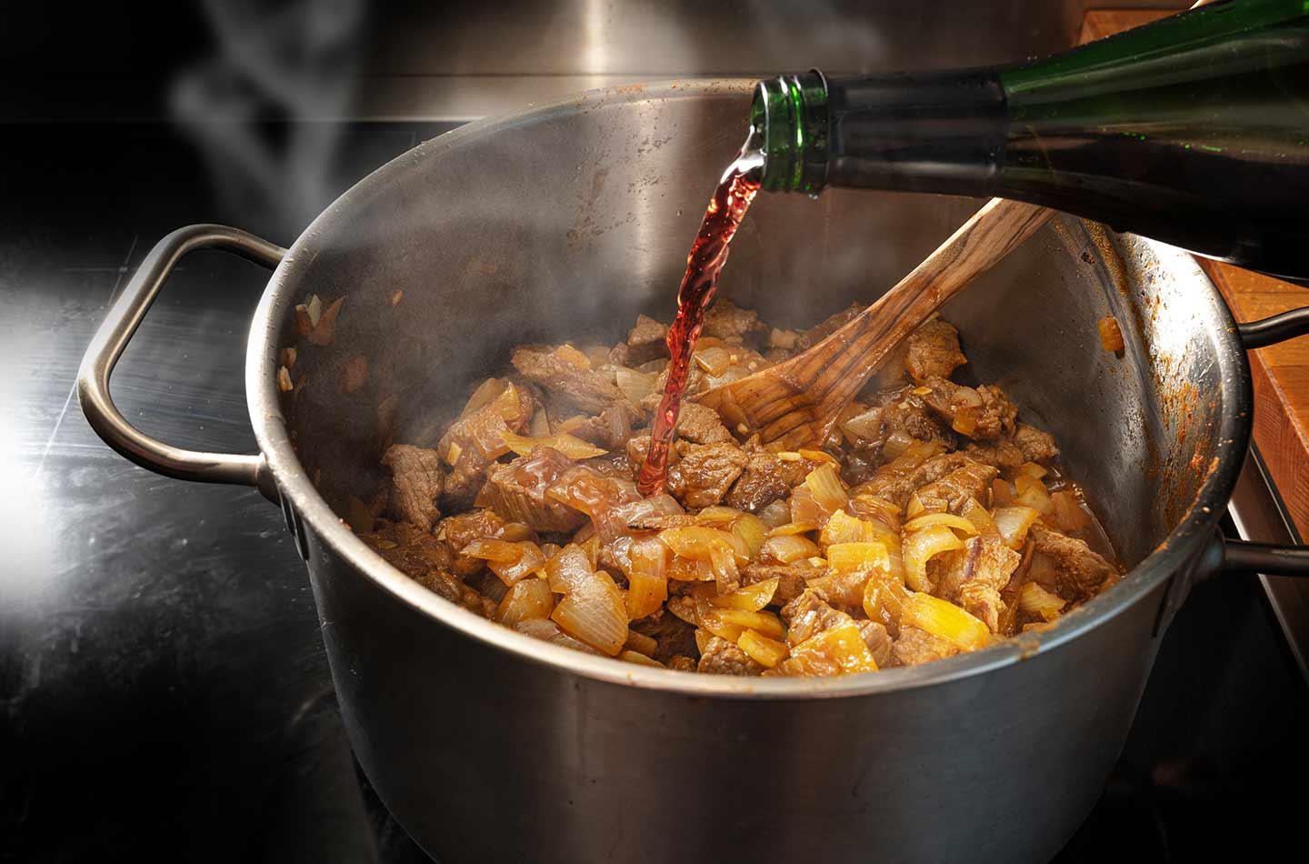 Rotwein wird in einen Kochtopf mit Fleisch und Zwiebeln gegossen.
