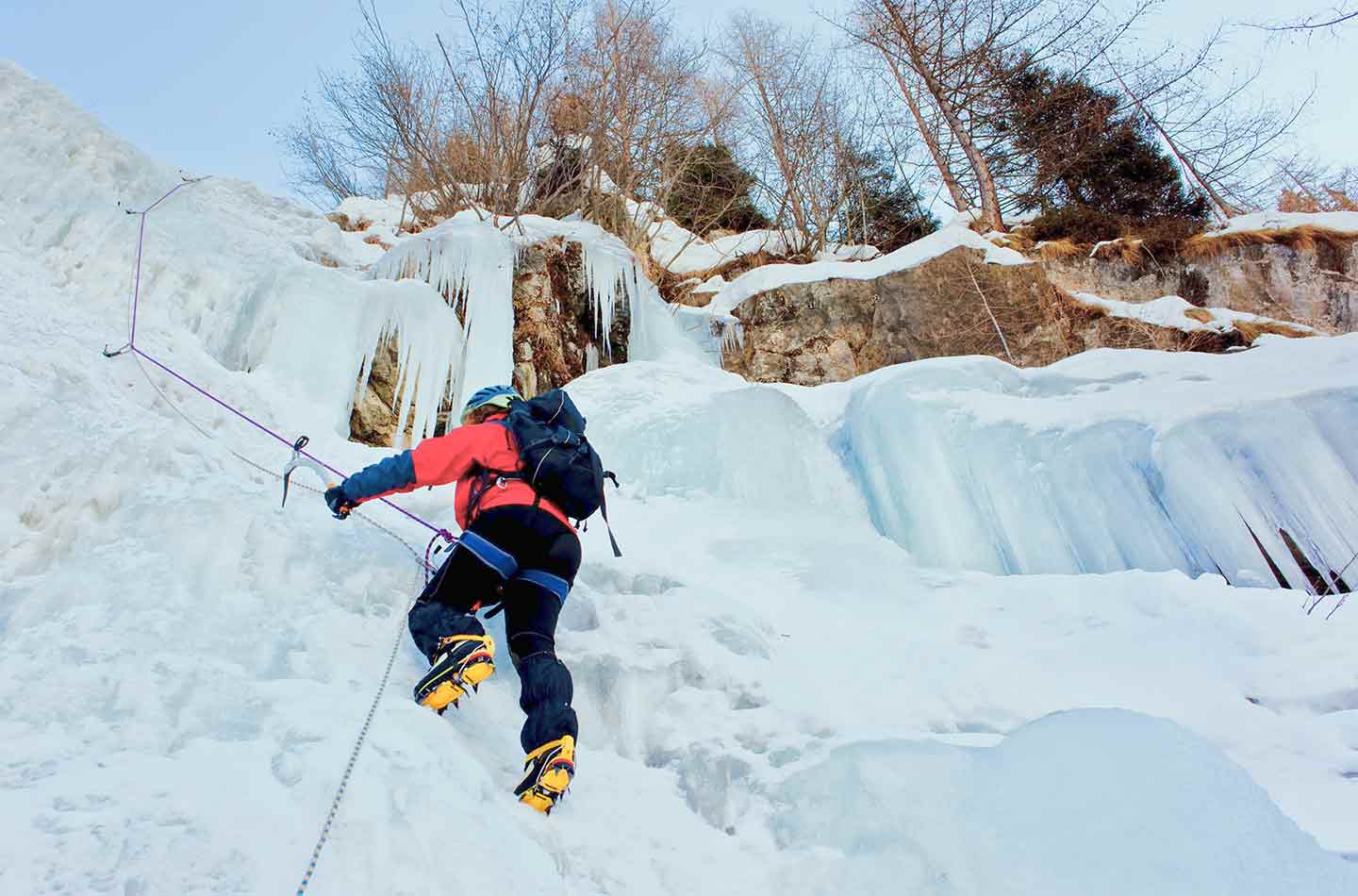 Mann in roter Jacke und mit Rucksack klettert an Eiswand.