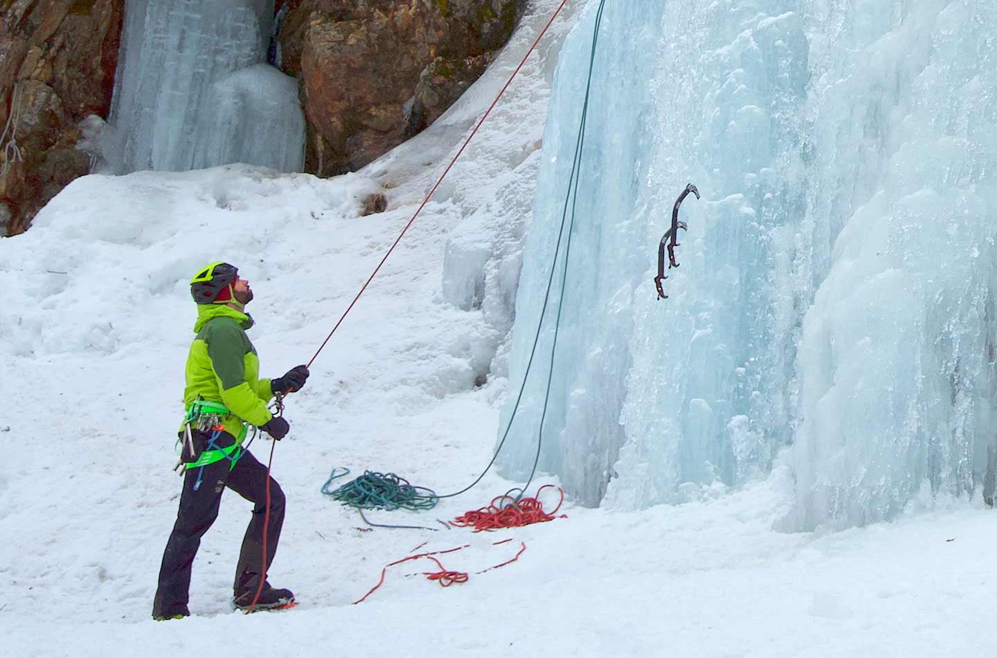 Mann in grüner Jacke sichert an der Eiswand.