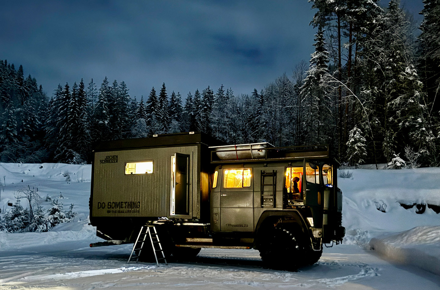 Truck beleuchtet in der Dunkelheit. Im Hintergrund Schneelandschaft. 