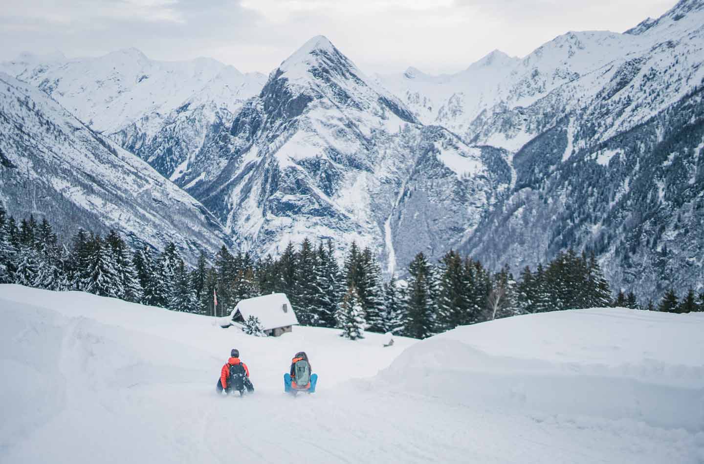 Rennrodel auf einer Piste mit Bergen und einer Hütte im Hintergrund