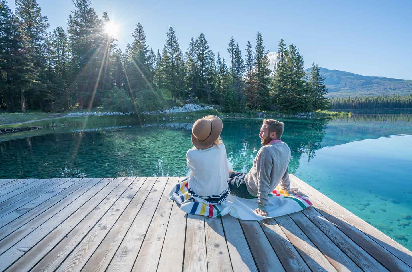 Paar sitzt auf einem Steg am See und genießt das schöne Wetter