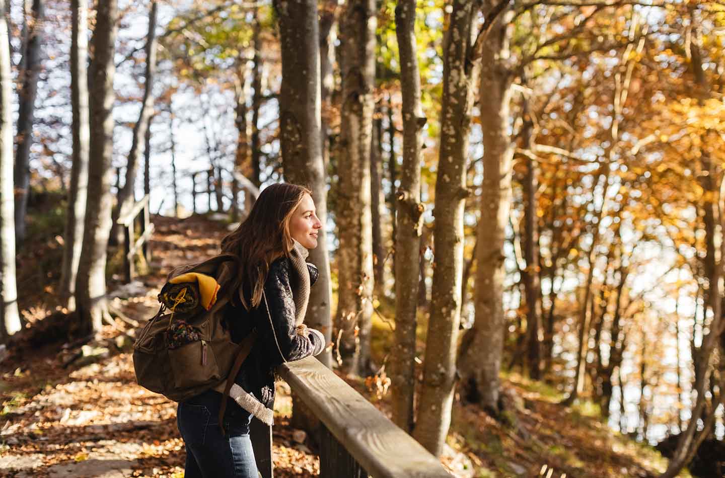 Eine Frau steht im Wald an einem Geländer und genießt den Herbst.