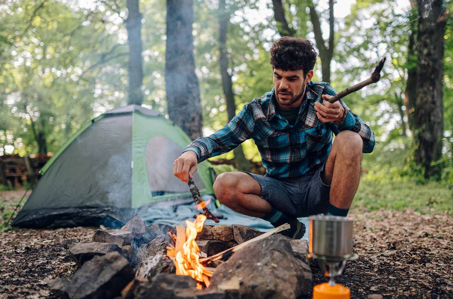 Mann sitzt im Wald und macht ein Lagerfeuer