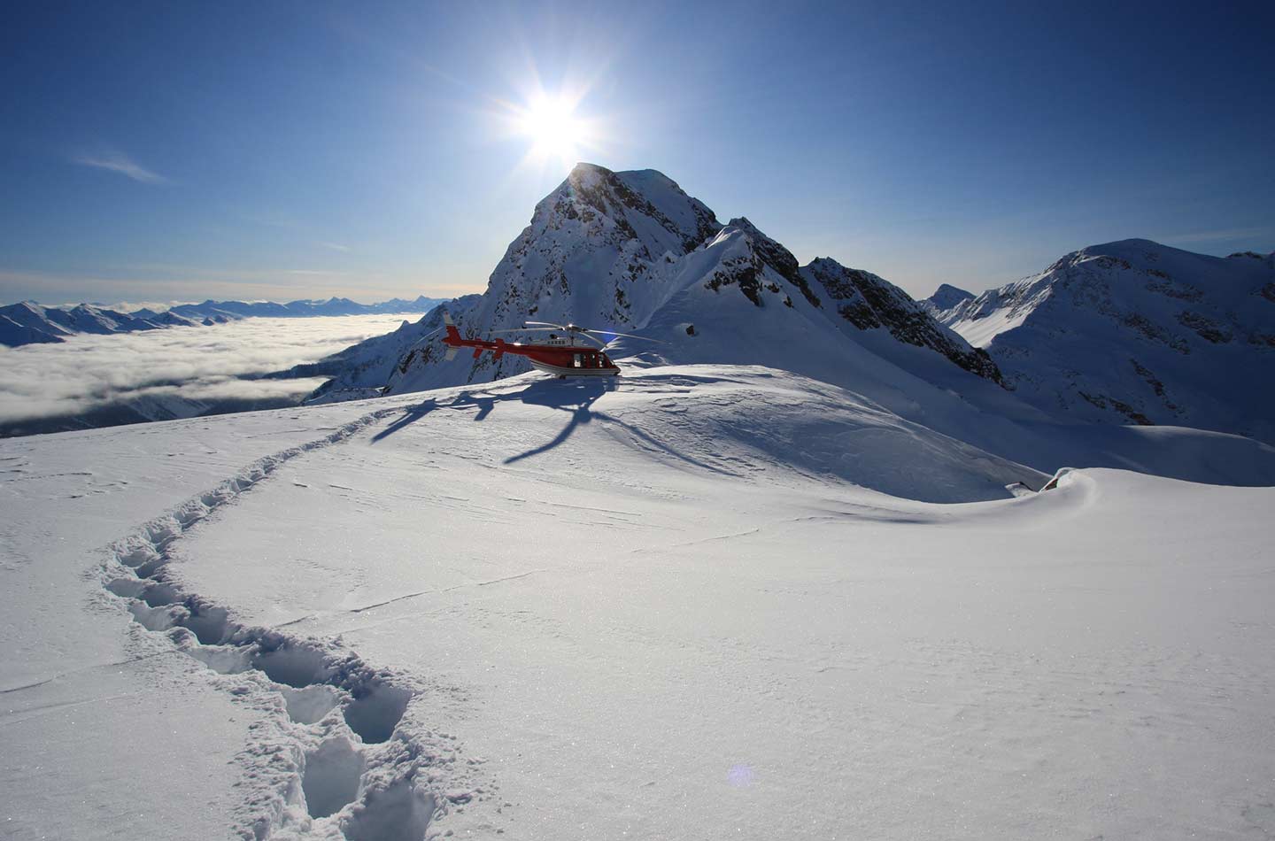 Ein Hubschrauber auf einer Bergkuppe mit der Sonne im Hintergrund.