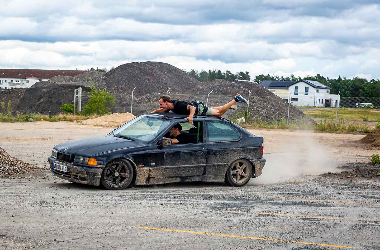 Ein Mann hält sich an einem Autodach fest, während das Auto fährt.