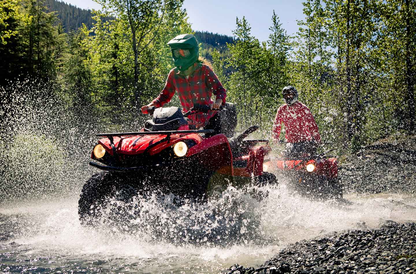 Zwei Leute fahren mit Quads durch einen flachen Fluss