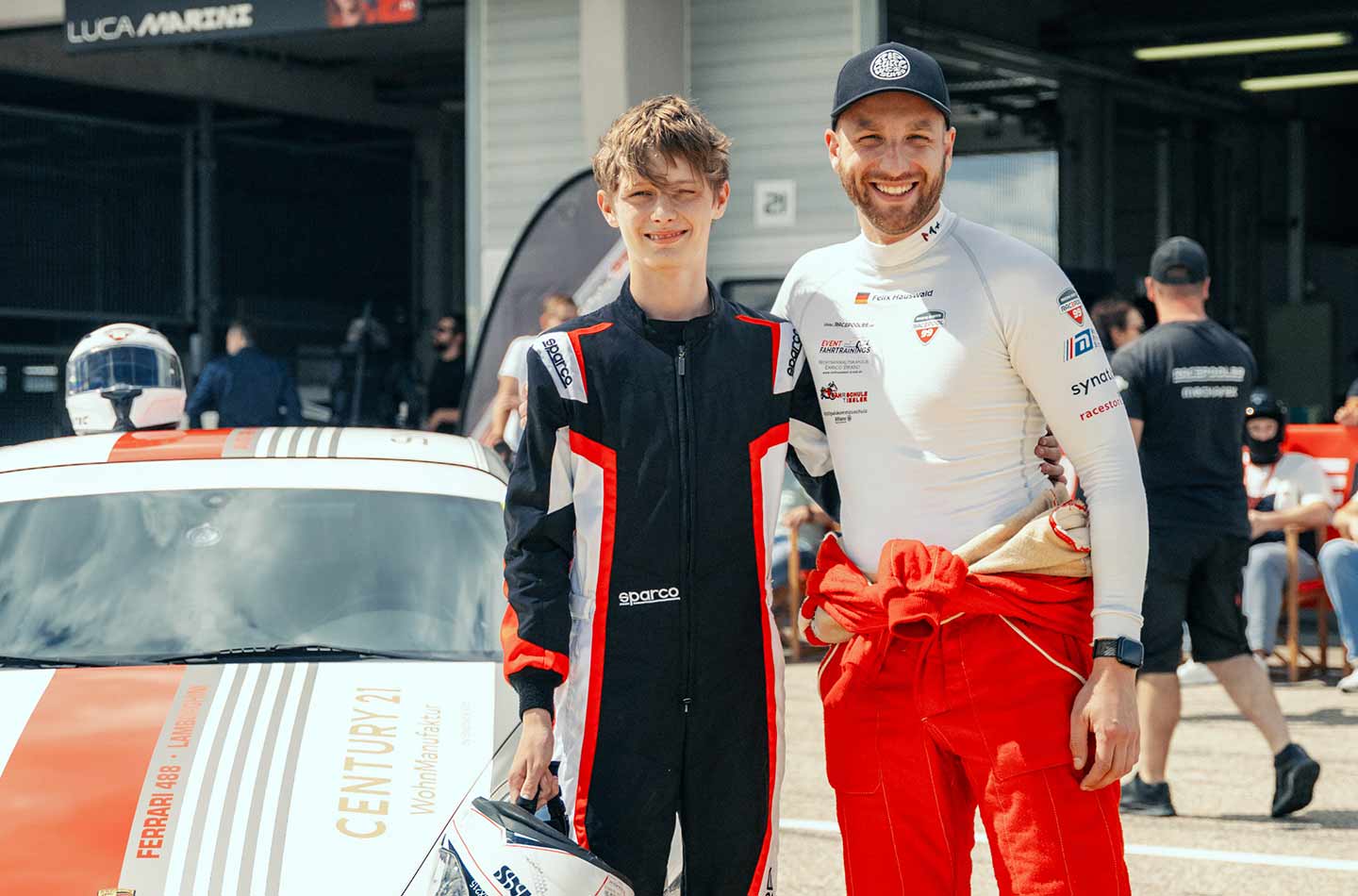 Ein Mann und ein Jungendlicher stehen in Rennoutfits auf einer Rennstrecke