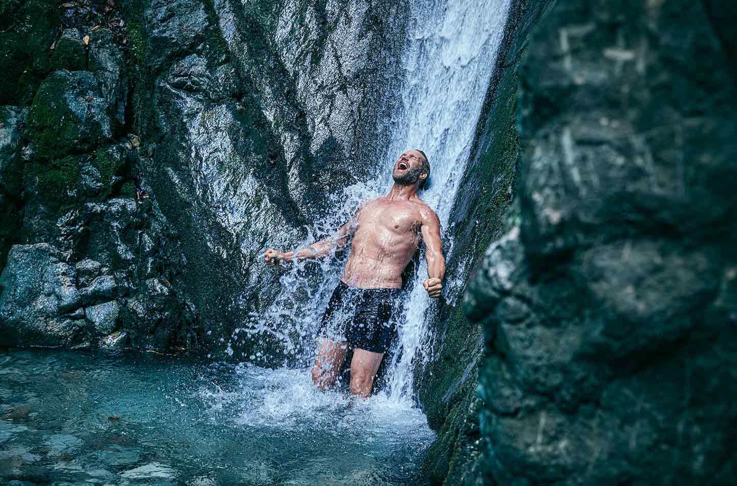 Ein Mann duscht sich unter einem natürlichen Wasserfall